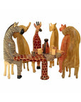 A set of hand-carved wooden animals, including representations of a zebra, giraffe, elephant, and others, seated around a table with patterned wooden glassware
