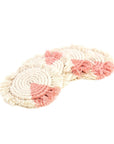 A set of four blush pink macrame coasters with fringe on a white background
