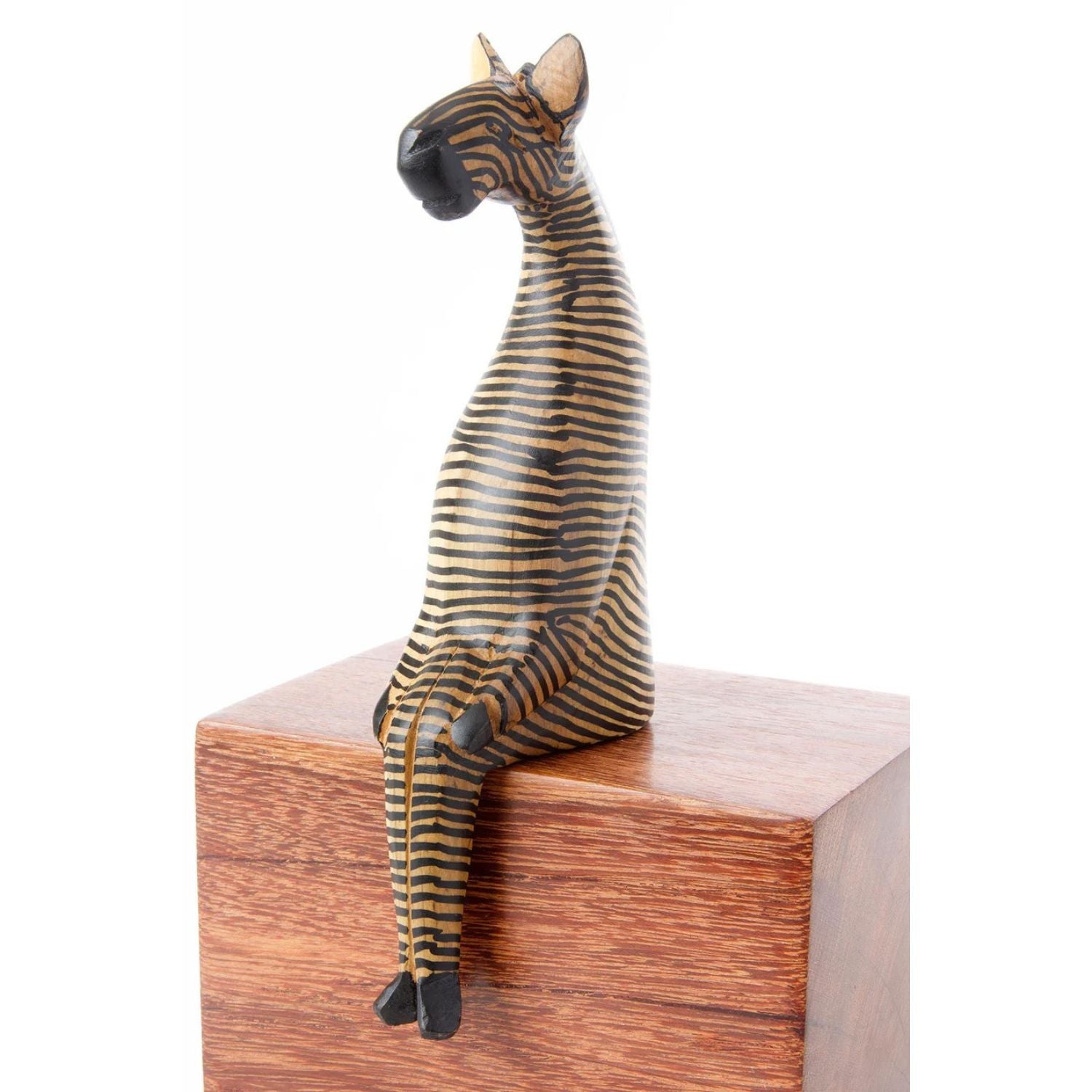 A handcrafted wooden zebra sculpture with hand painted stripes, perched on a wooden shelf.