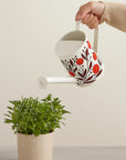 Person watering a plant with a decorative floral design watering can on a plain background