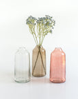 Three glass vases of different colors with a single stem of flowers on a white background