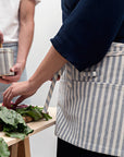 A person wearing a blue waist apron with multiple pockets and a utility loop touching lettuce.