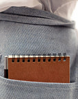 The backside of a blue waist apron with multiple pockets and a utility and one of the pockets holding a notepad.