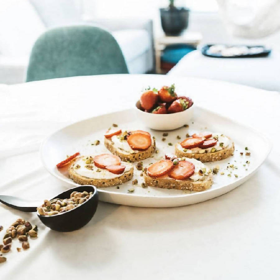A white ceramic serving platter with toast and a bowl of fruit on top