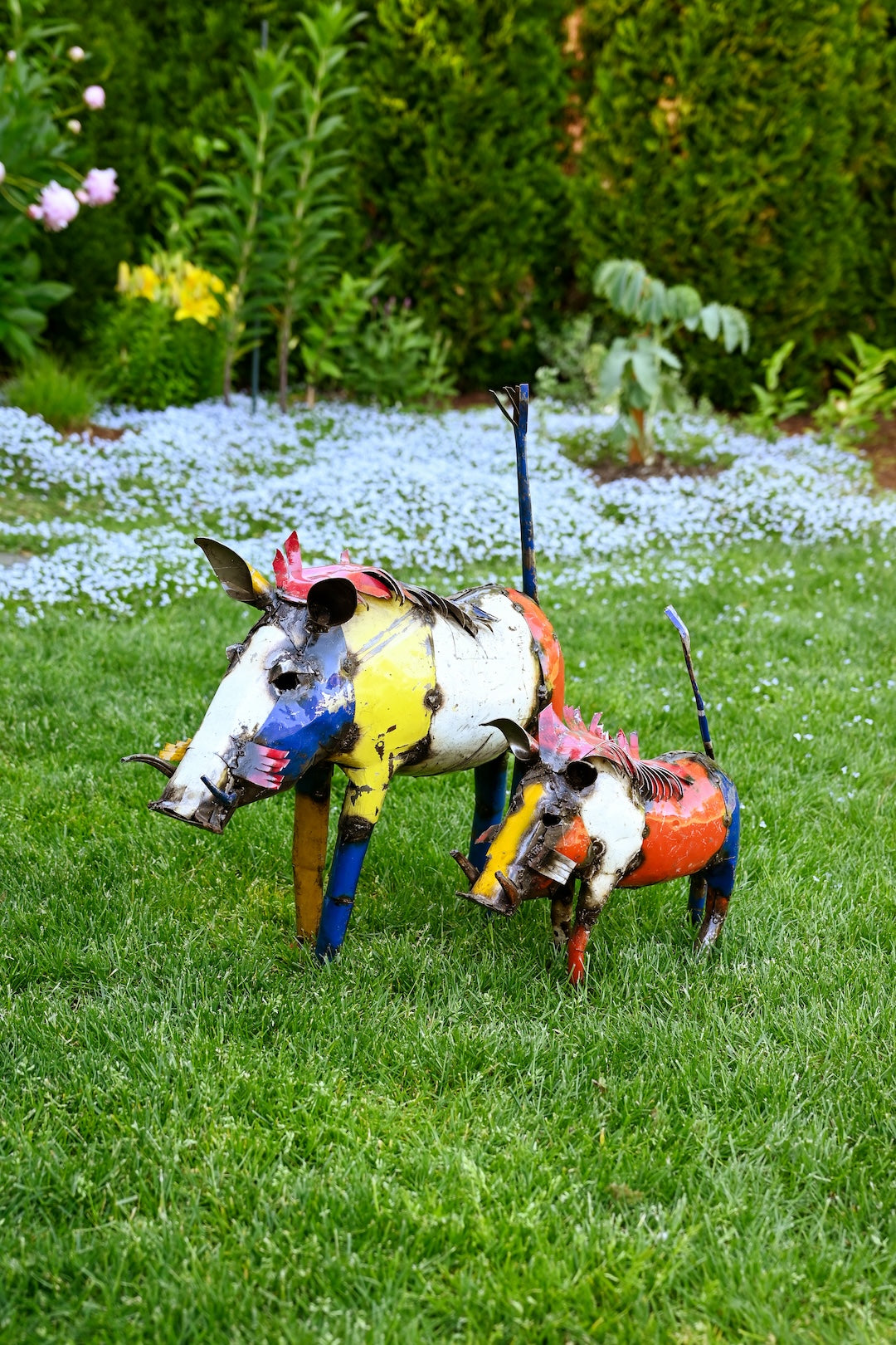 Colorful metal sculptures of pigs on a grassy lawn with flowers and plants in the background