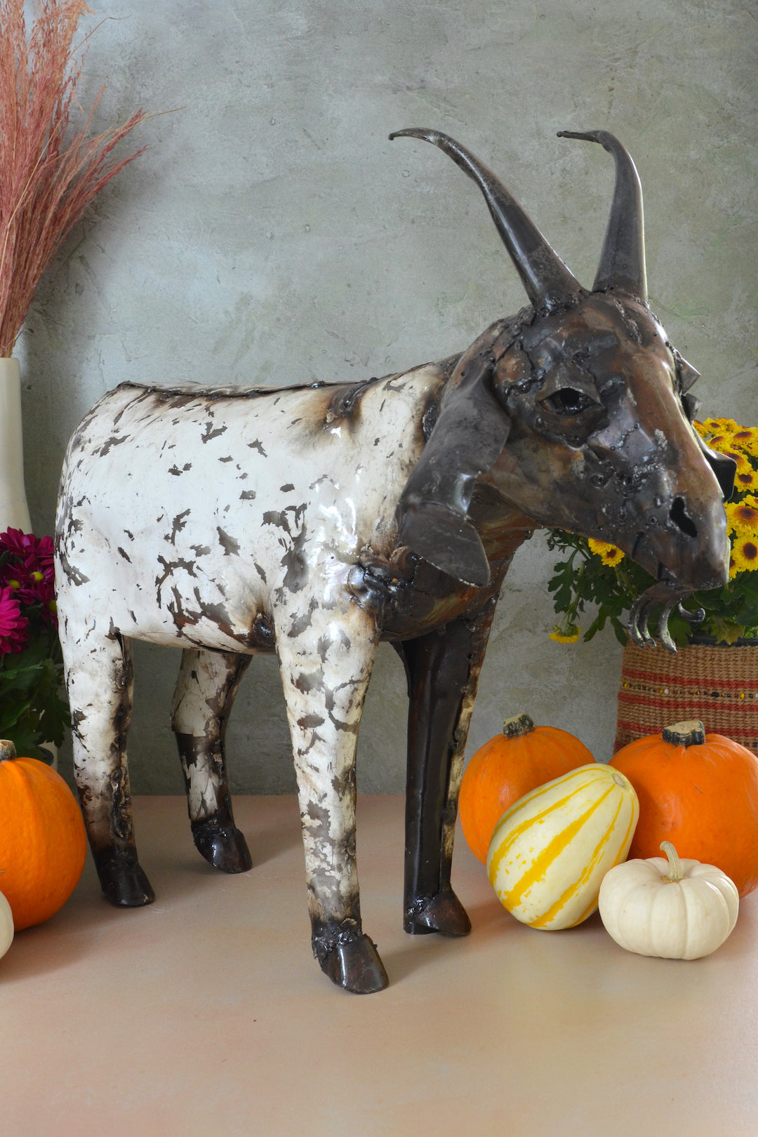 Decorative goat sculpture with autumn-themed pumpkins and flowers on a neutral background