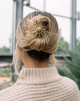 Person with blonde hair styled in an updo with a decorative hairpin, wearing a beige sweater.