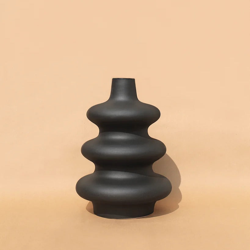 A black, contour-shaped ceramic vase on a plain background.