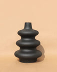 A black, contour-shaped ceramic vase on a plain background.