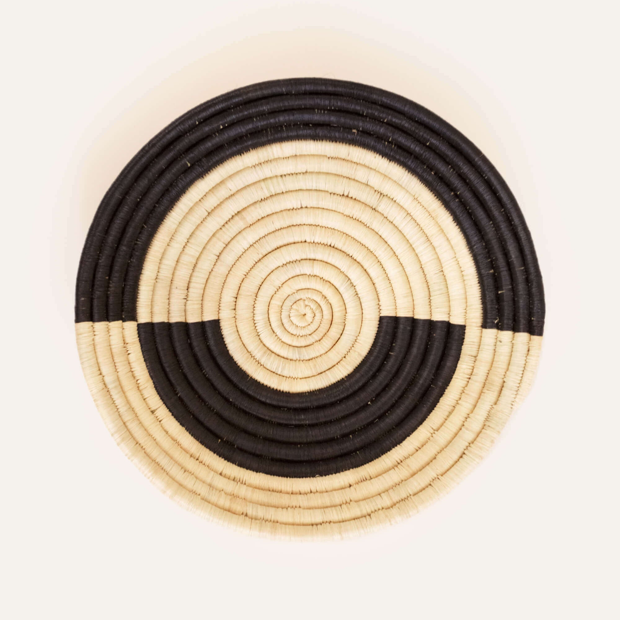 Handcrafted circular basket with concentric bands of beige and black, with a loop for hanging at the back