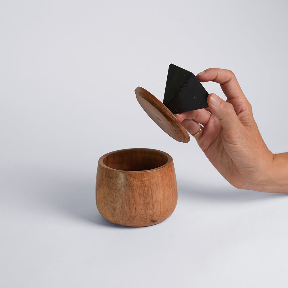 Wooden cup with a hand holding a black triangle-shaped object on a light gray background