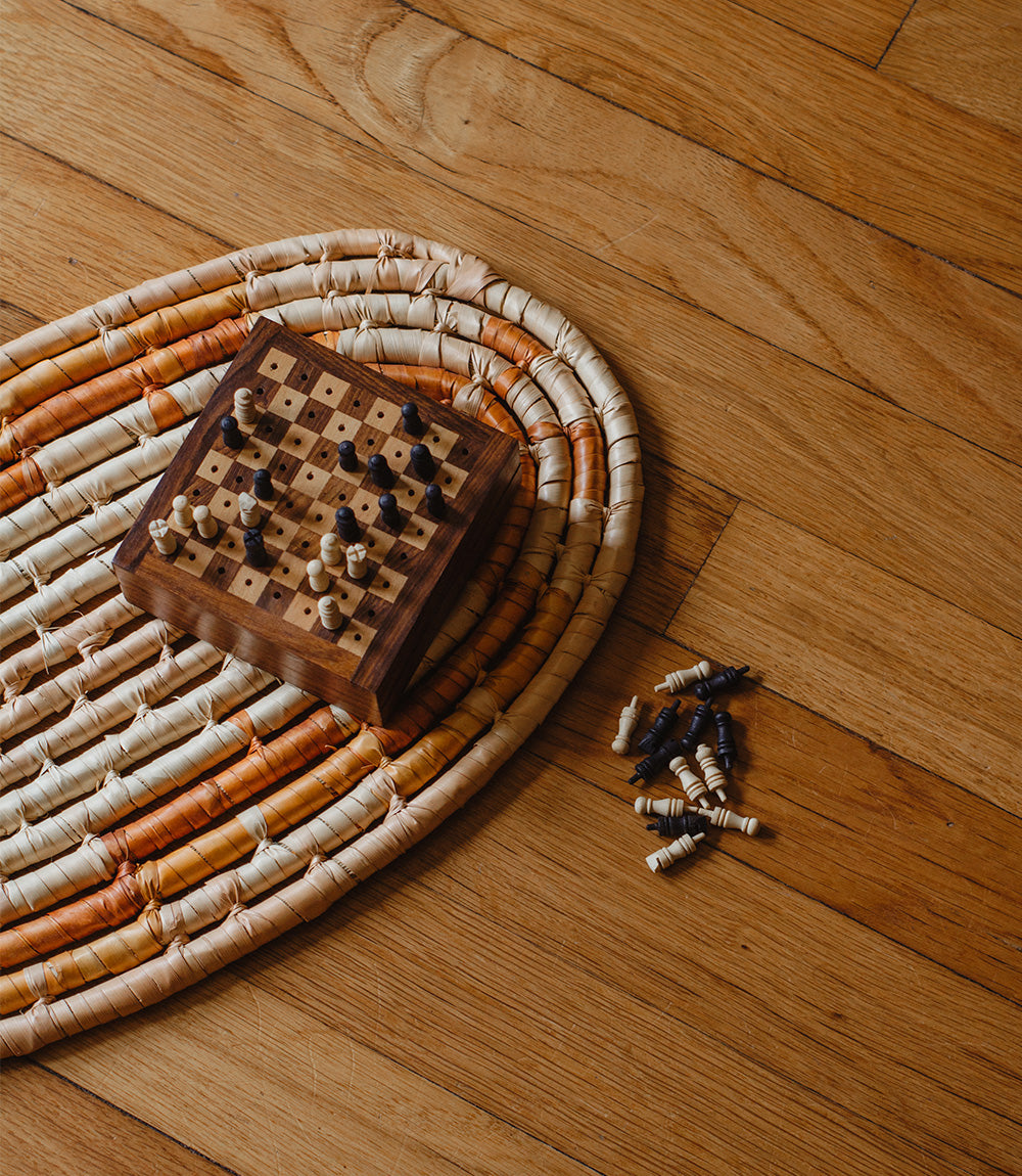 A portable wooden chess game with pieces carved from Indian rosewood, displayed on a carpet on a wooden floor.