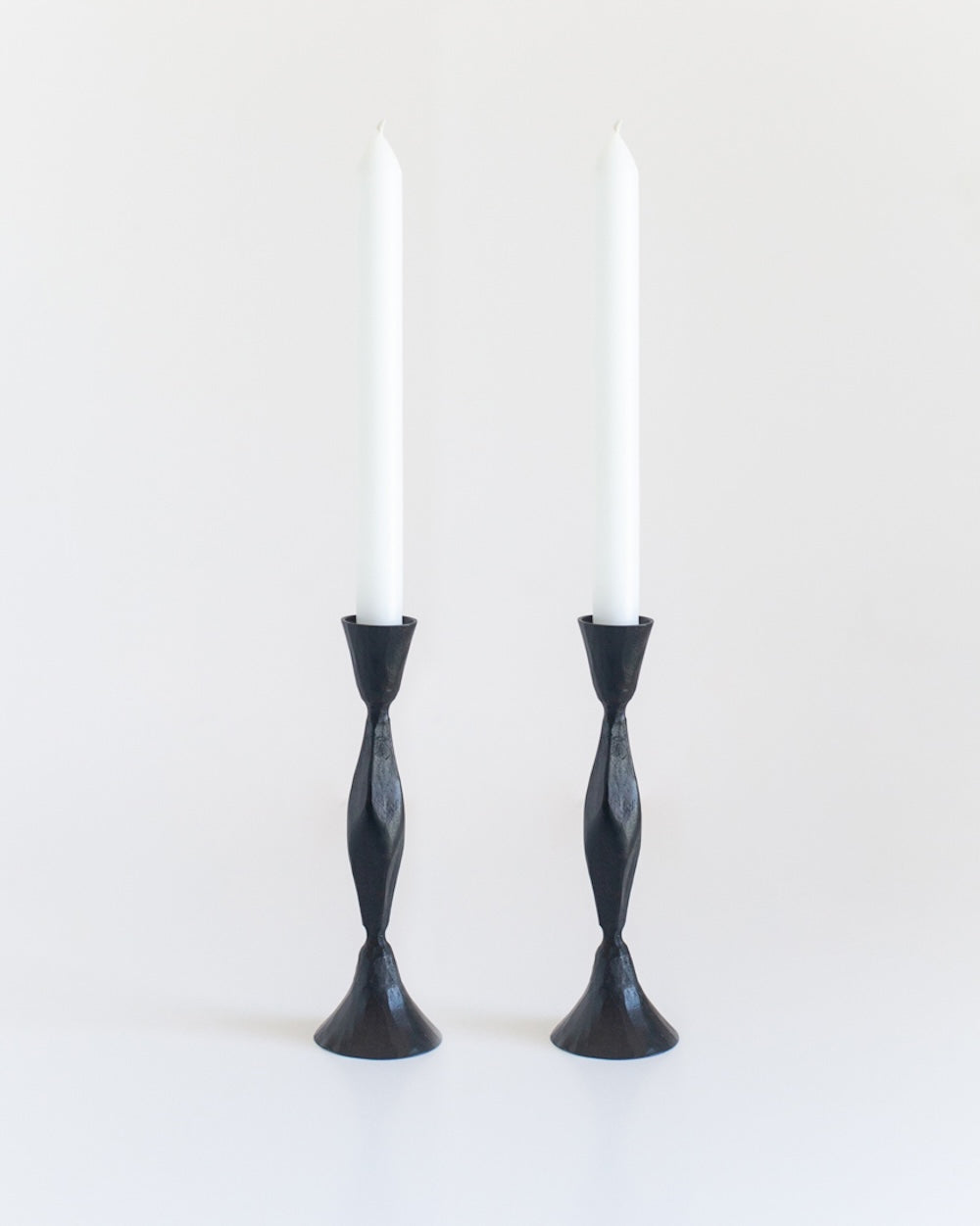 Two black candle holders with white candles on a white background