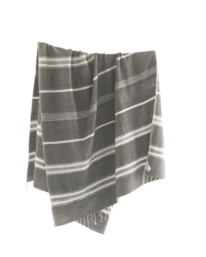 A gray and white striped cotton throw blanket with fringes, laid out and draped