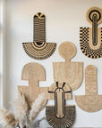 Multiple woven abstract wall masks with geometric patterns displayed on a white wall