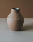 A handcrafted ceramic vase with a rounded body and a narrower top, presented in a muted brown color, placed on a flat surface.