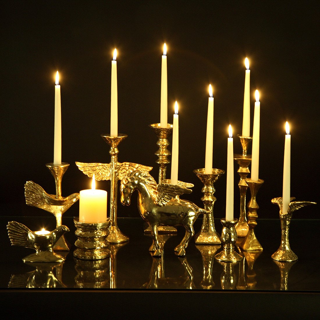 Decorative candle holder with winged creatures and lit candles on a reflective surface.