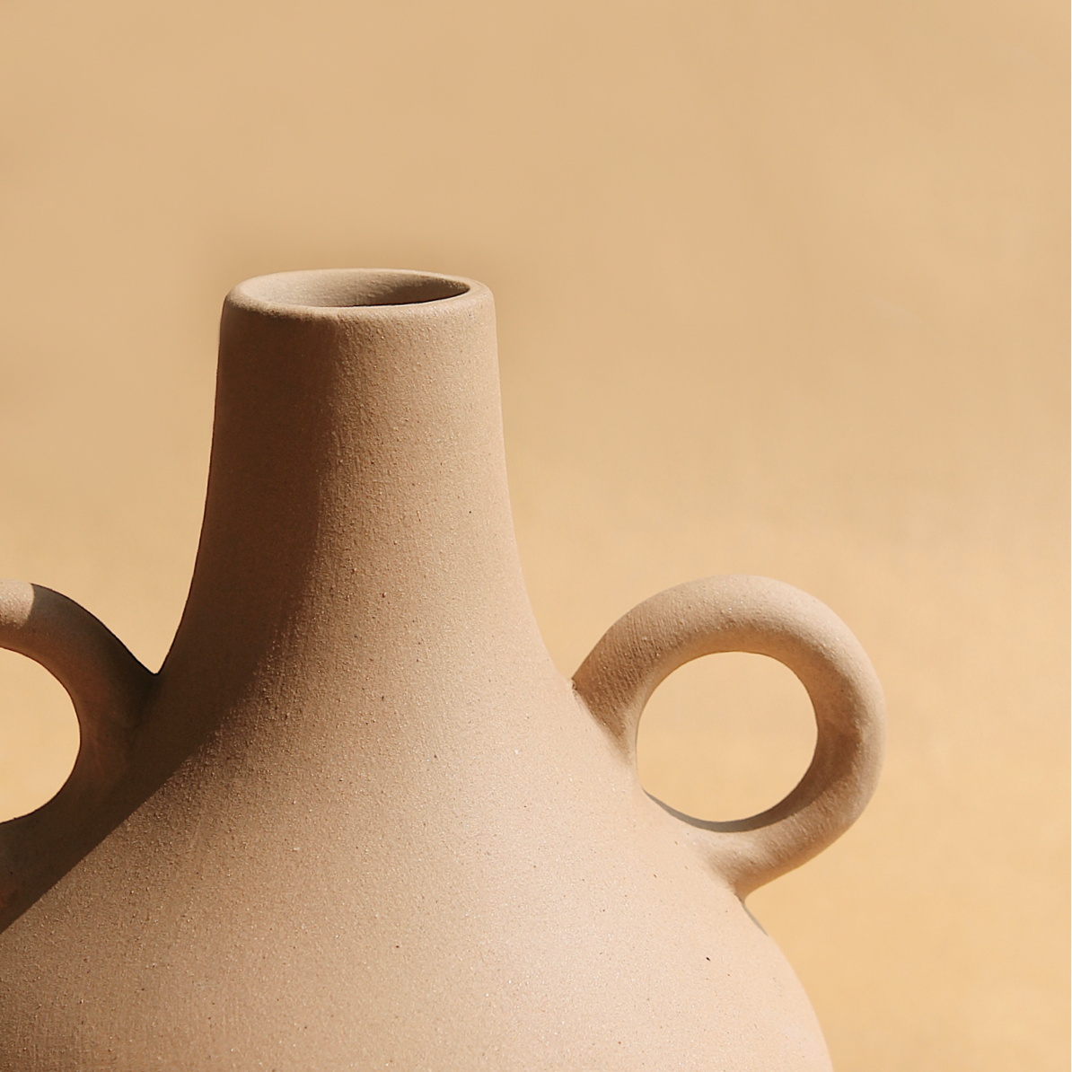 A beige ceramic vase with a traditional Harappan shape and two circular handles on the sides.