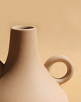 A beige ceramic vase with a traditional Harappan shape and two circular handles on the sides.