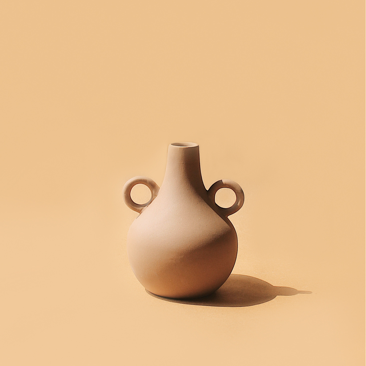 A beige ceramic vase with a traditional Harappan shape and two circular handles on the sides.