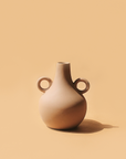 A beige ceramic vase with a traditional Harappan shape and two circular handles on the sides.