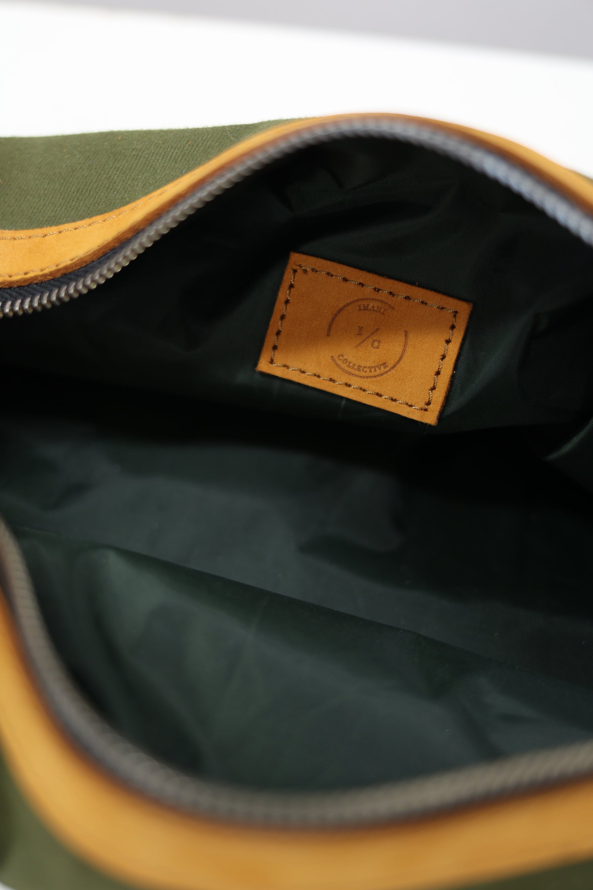 An unzipped green toiletry bag with leather accents and a metal zipper.