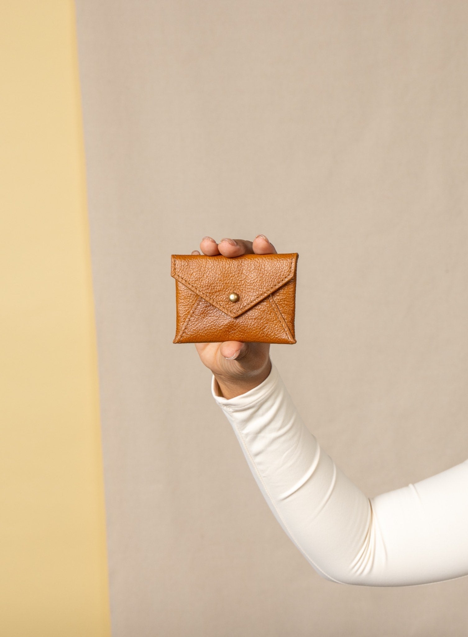 Person holding a brown leather wallet against a beige background