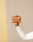 Person holding a brown leather wallet against a beige background