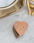 A heart-shaped pink marble keepsake box with brass stars inlay on the lid, set on a wooden base on a marble table