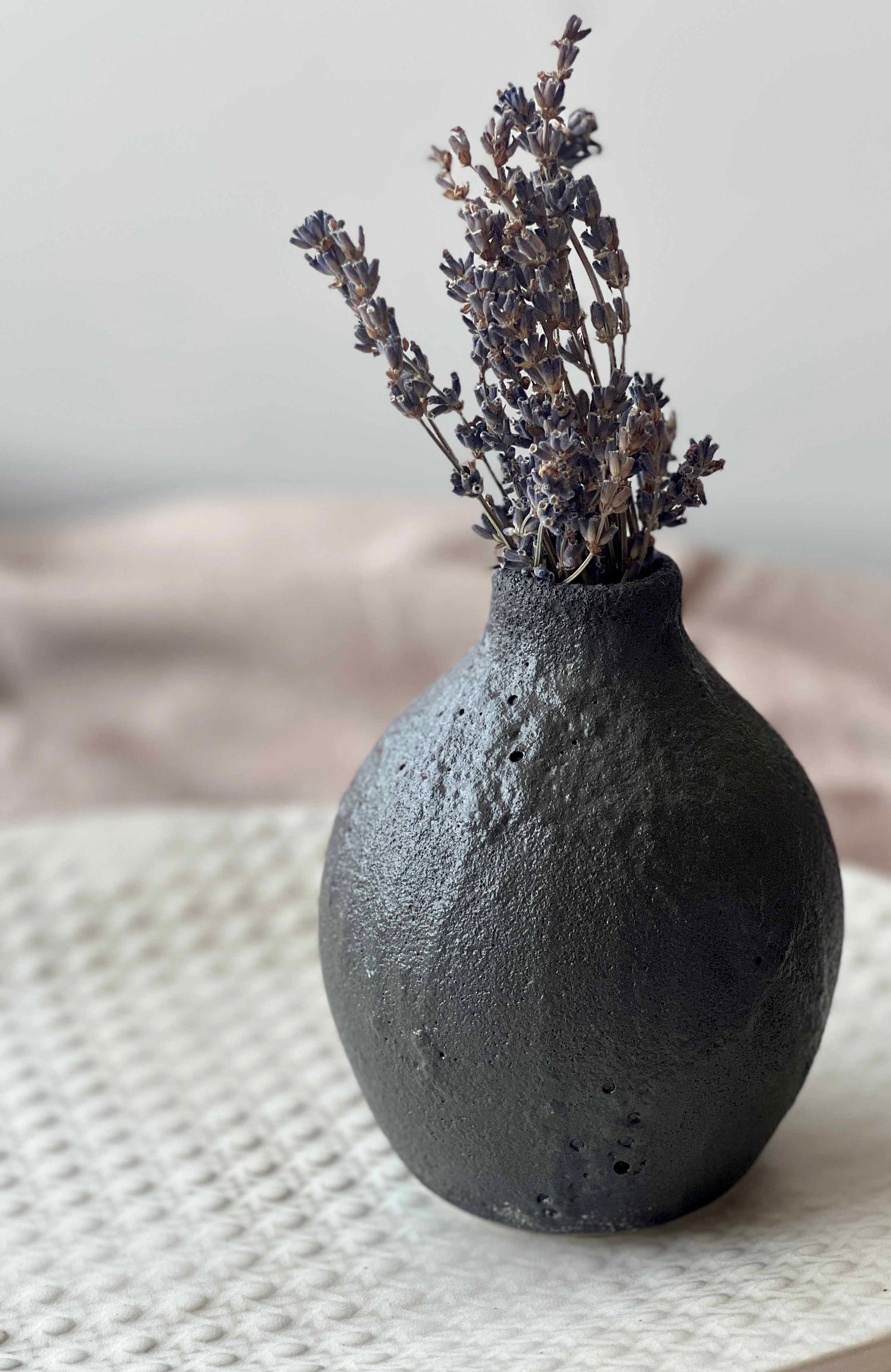 Black textured vase with dried lavender on a textured surface