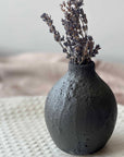 Black textured vase with dried lavender on a textured surface