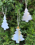 Three white tree-shaped ornaments hanging on a green bush