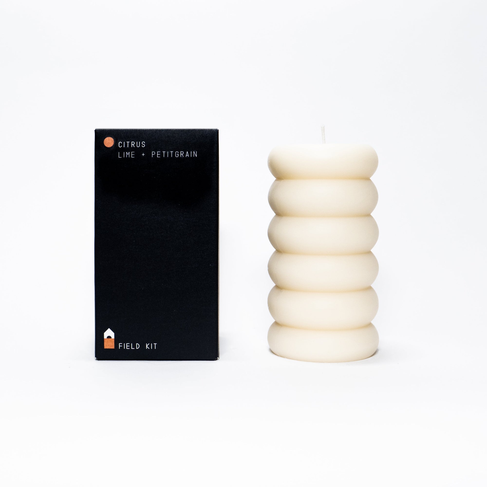 A sculptural pillar candle designed for burning, shown alongside its packaging which indicates the fragrance: bergamot, Persian lime, and petitgrain.