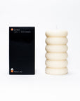 A sculptural pillar candle designed for burning, shown alongside its packaging which indicates the fragrance: bergamot, Persian lime, and petitgrain.