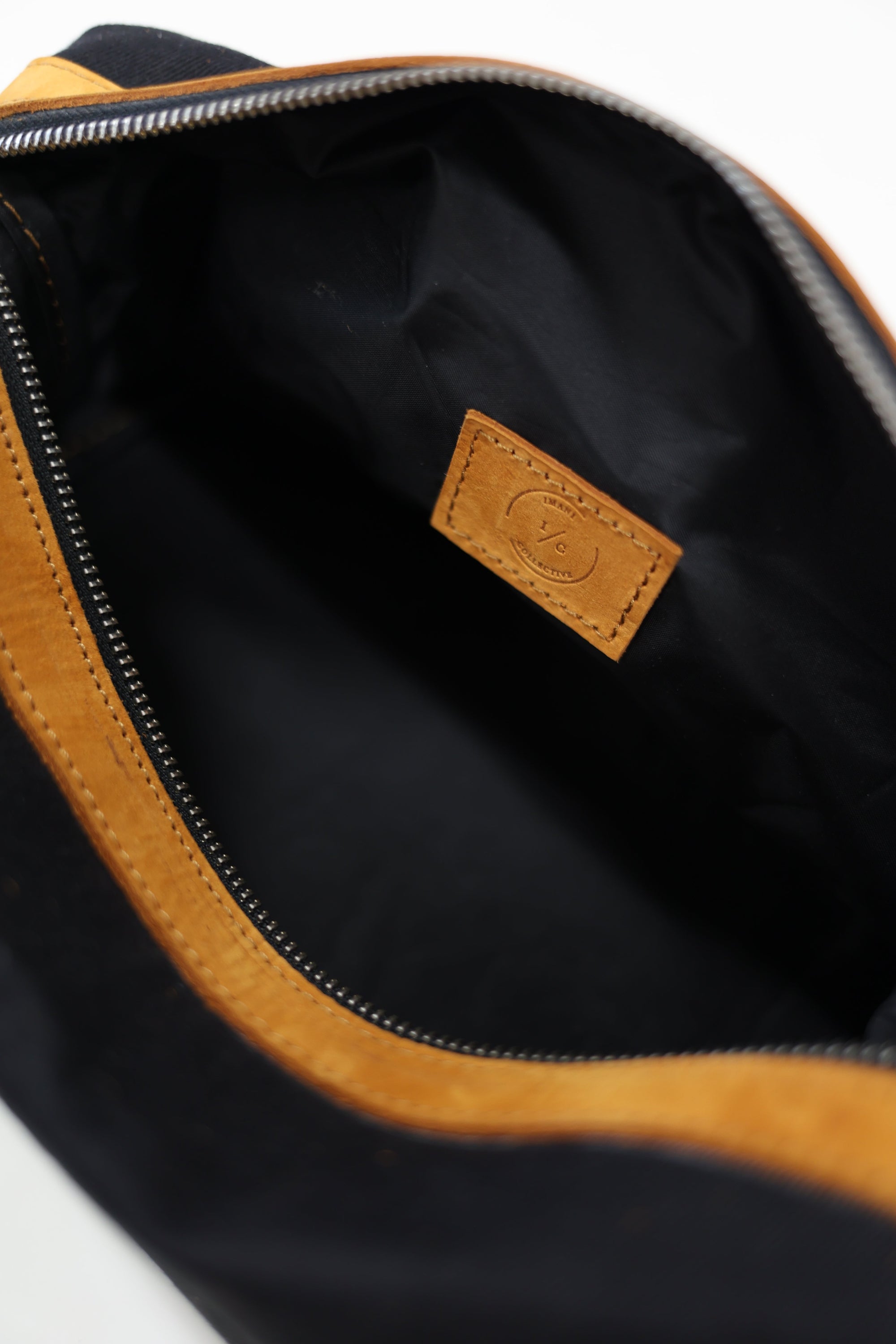 An unzipped black toiletry bag with a yellow zipper and leather details on a white background.