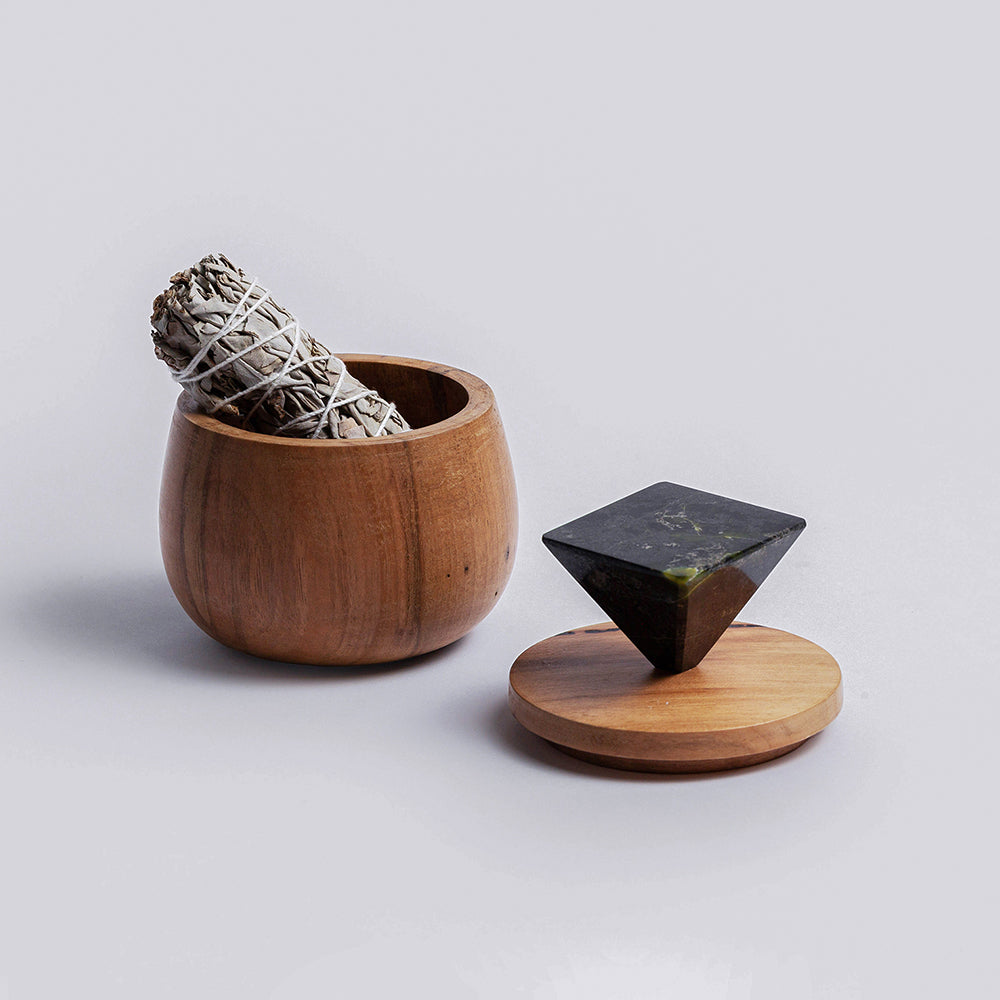 Wooden container with smudge stick and black geometric sculpture on a light gray background