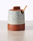Ceramic honey pot with textured surface and wooden spoon on a light background