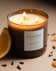 Scented candle labeled 'Slow North' with orange and clove elements on a neutral background
