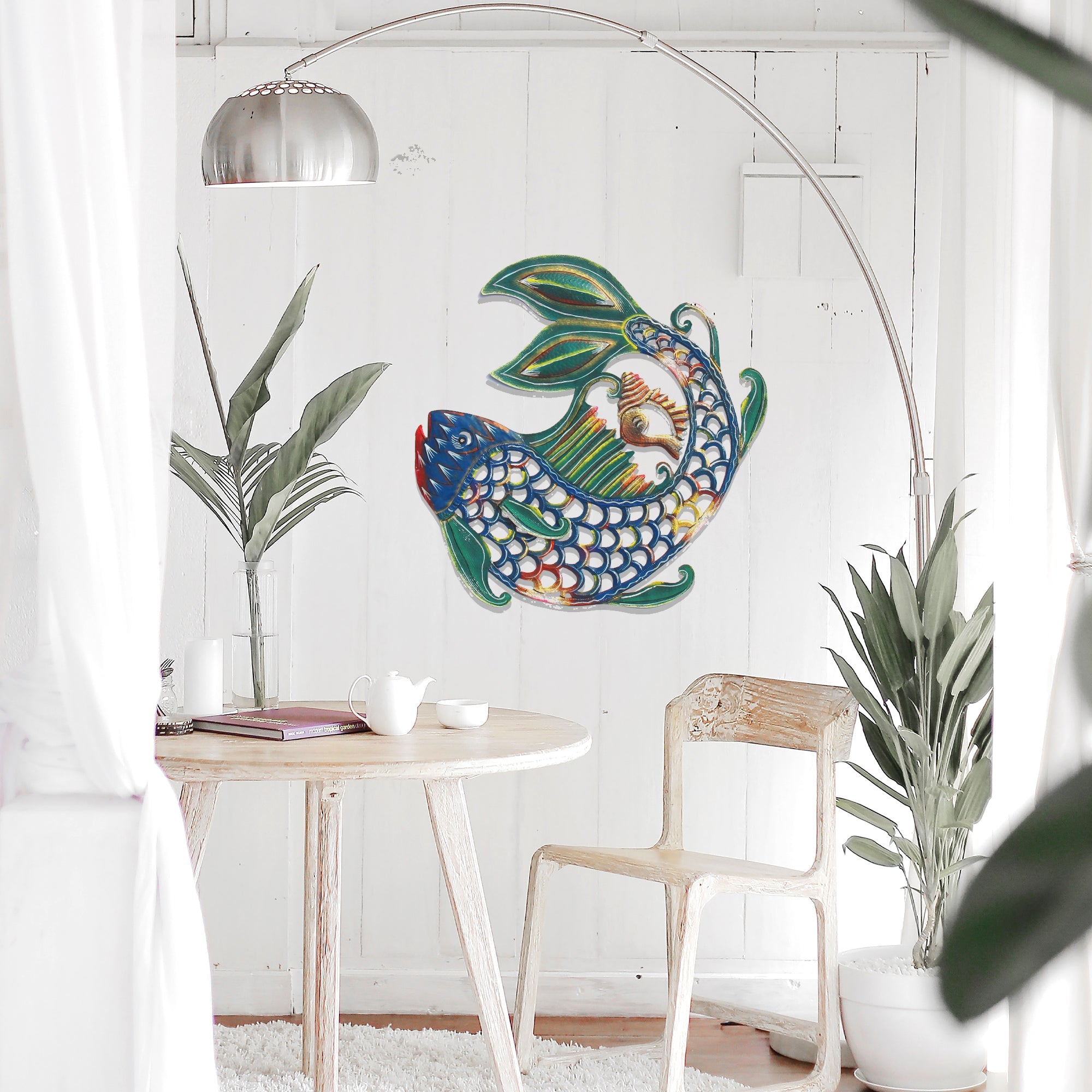 A handmade metal wall art piece depicting a fish with shell-like patterns hanging on a white wall
