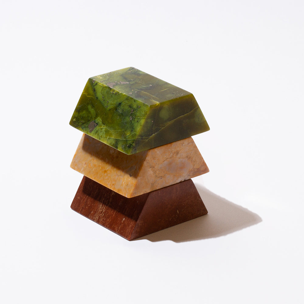 The three pieces of a a triangular sculpture of different colored gemstones, stacked on top of each other on a white background.