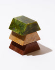 The three pieces of a a triangular sculpture of different colored gemstones, stacked on top of each other on a white background.