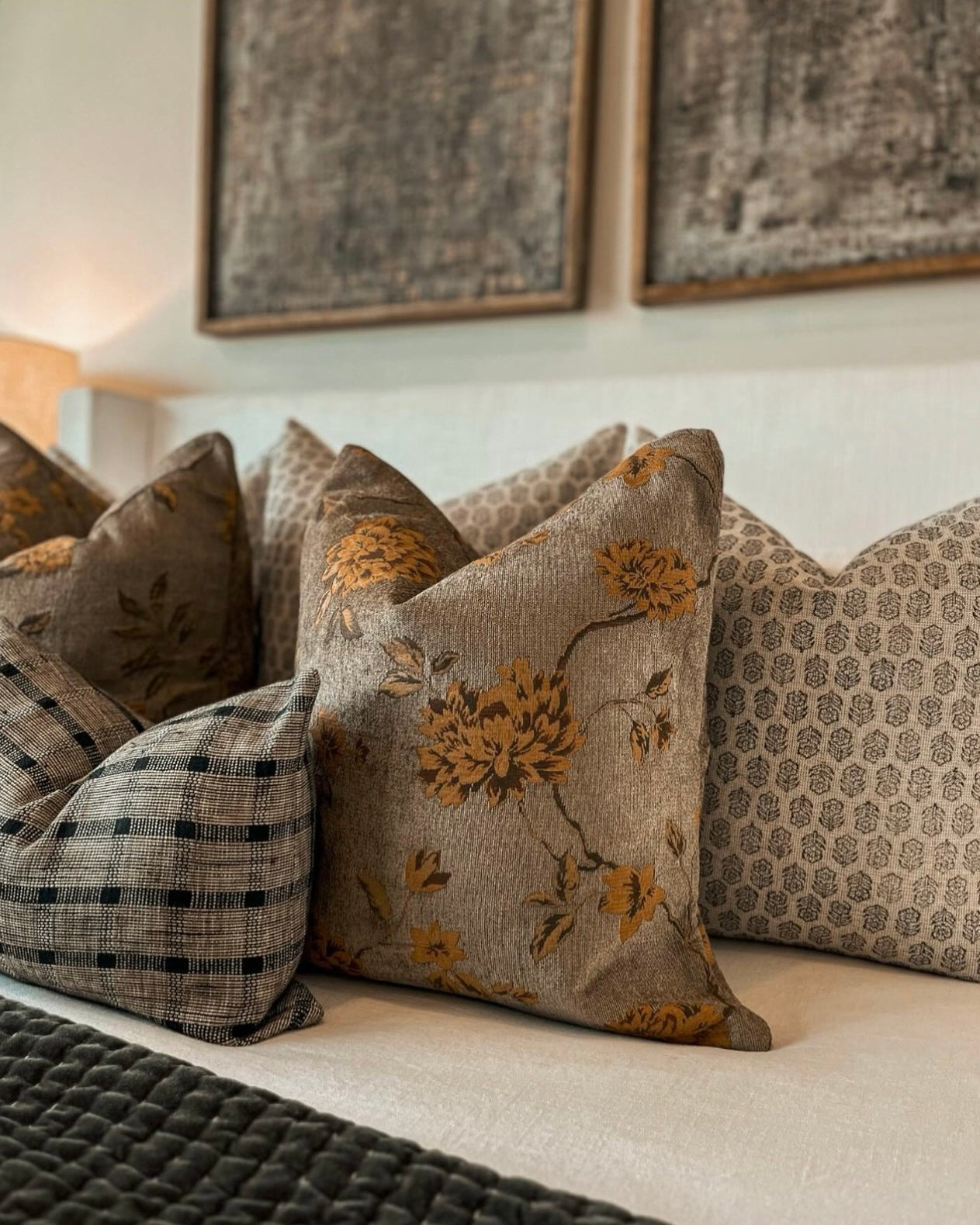 Decorative pillows on a sofa with floral patterns and checkered designs, framed artwork in the background