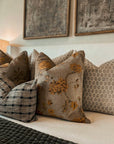 Decorative pillows on a sofa with floral patterns and checkered designs, framed artwork in the background