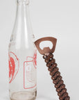 Bottle opener with chain design next to a clear bottle on a white background
