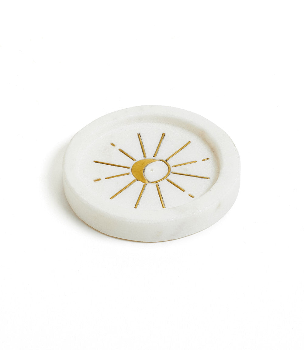 A round white marble incense holder with a gold radiating moon design in the center.
