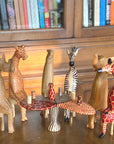 A set of handmade wooden animals surrounding a table on a wooden table