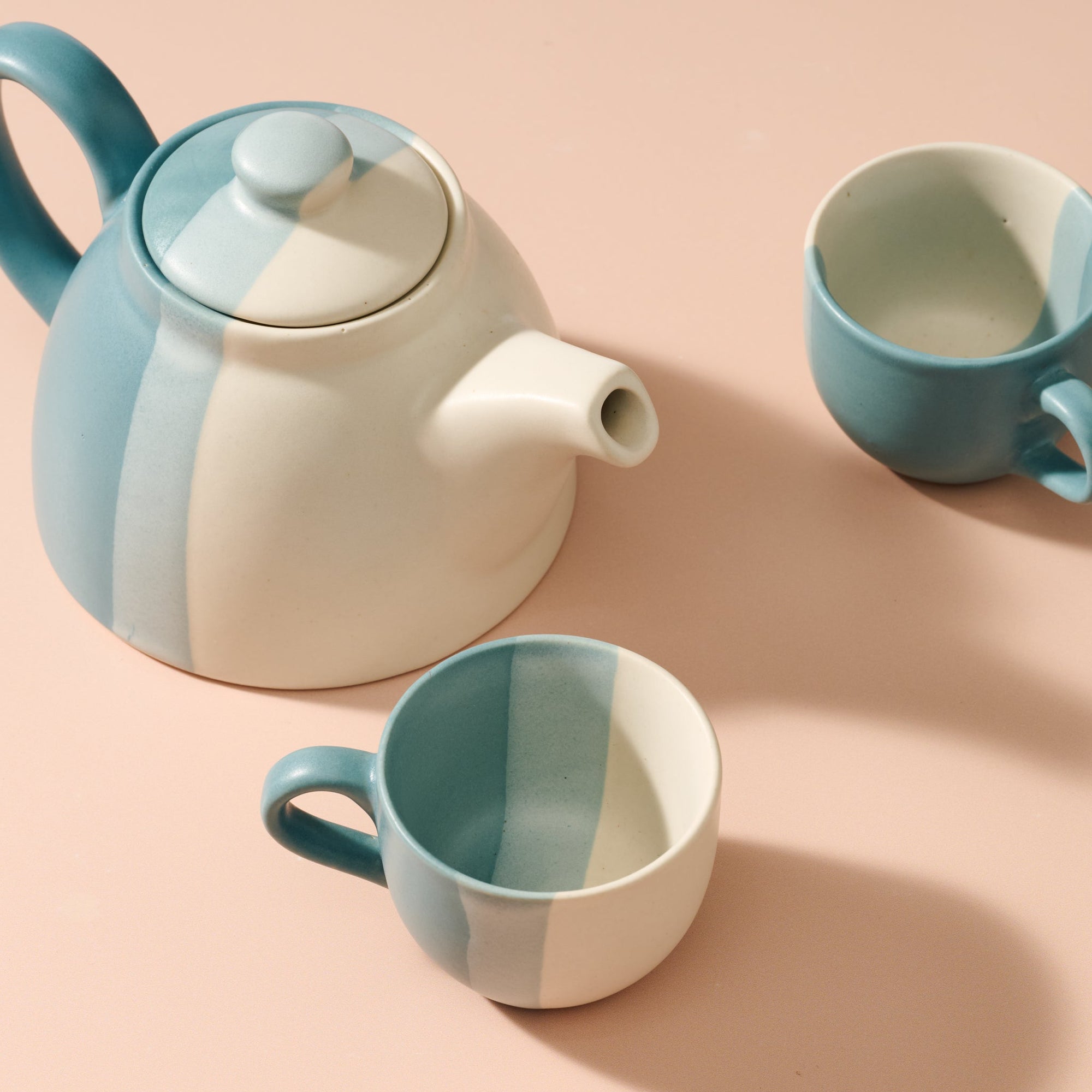 Ceramic teapot and two mugs with a geometric color block design on a peach background