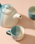 Ceramic teapot and two mugs with a geometric color block design on a peach background