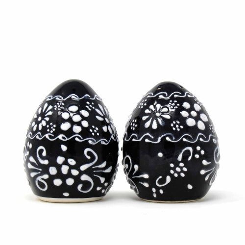 A pair of handmade pottery spice shakers, one with a single hole at the top and the other with five holes, featuring a black body with white floral patterns