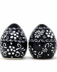 A pair of handmade pottery spice shakers, one with a single hole at the top and the other with five holes, featuring a black body with white floral patterns